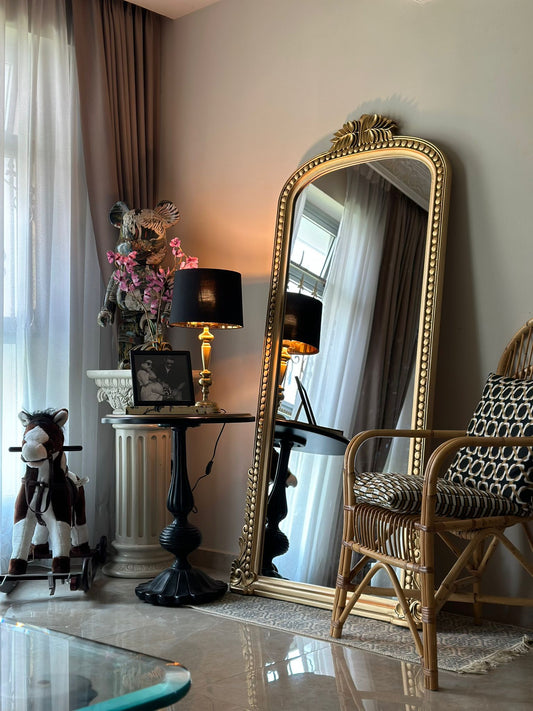 A large, hand-carved, rectangular mirror with a gold brass finish, placed in a living room setting.