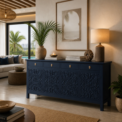 A navy blue carved wooden sideboard or credenza in a styled living room, decorated with a potted plant, books, a candle, a textured sculpture, and a table lamp.