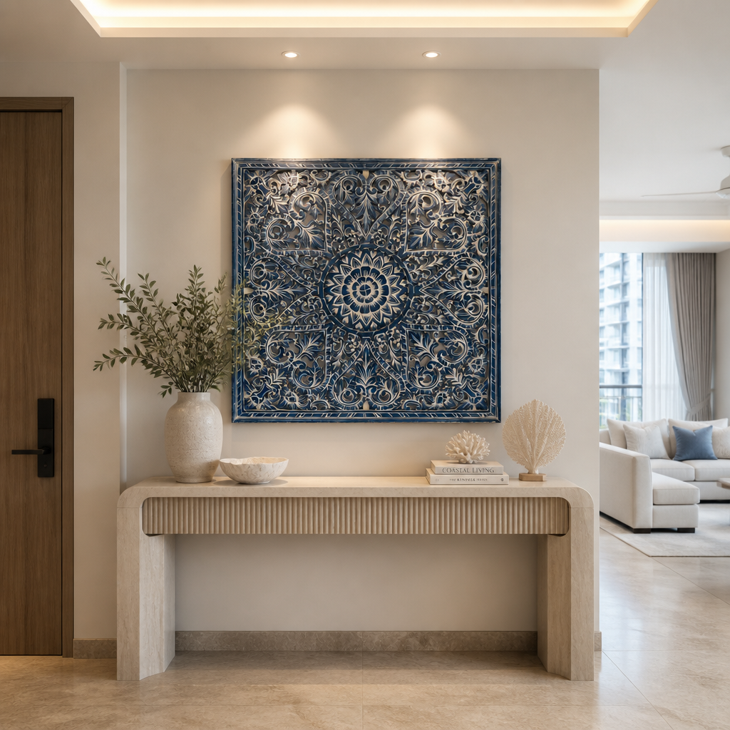 A large square wall art piece with an intricate navy blue and cream mandala-style pattern hangs above a light wood console table in a modern, well-lit living space.