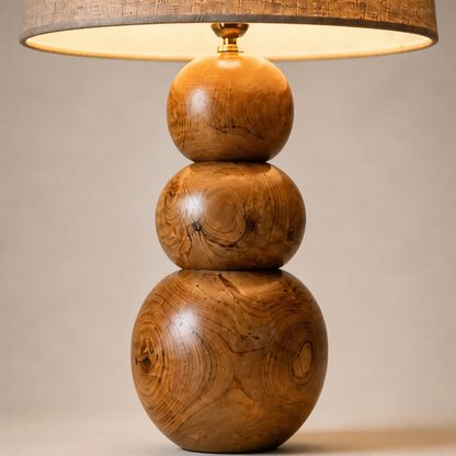 A three-tiered wooden table lamp with a tapered drum shade, featuring a polished wood base with prominent grain patterns in warm brown and golden tones.