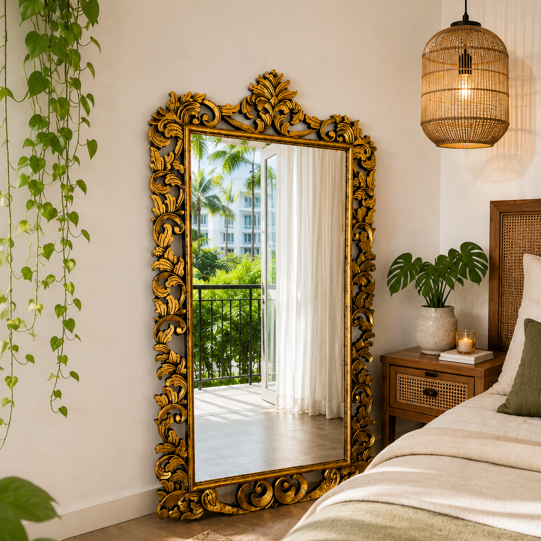 An ornate gold-framed floor mirror with intricate scrollwork stands in a styled bedroom next to a bed with neutral bedding, a woven rattan nightstand, a hanging woven pendant light, and a green trailing plant.