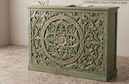 A carved wooden reception desk or cabinet with a distressed green finish and ornate floral detailing, shown in a room setting with a text overlay indicating custom order dimensions.